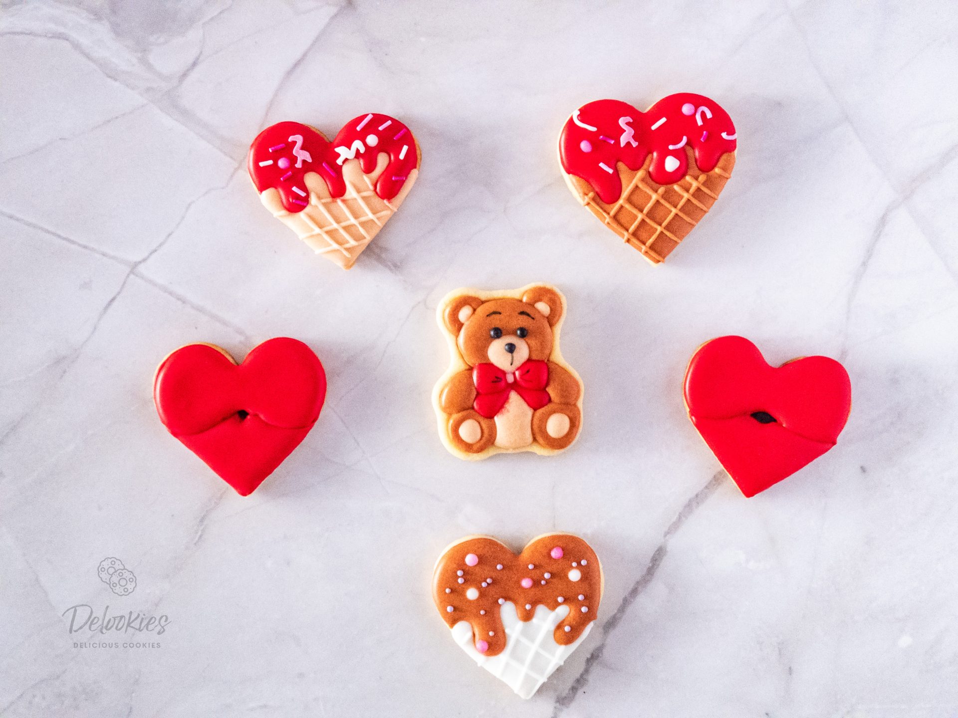 Beautifully crafted Valentine's-themed cookies from Delookies, featuring a charming teddy bear cookie, cone-inspired heart cookies with drizzled icing, red lips cookies, and a heart-shaped cookie with sprinkles, all decorated with smooth and decorative icing.