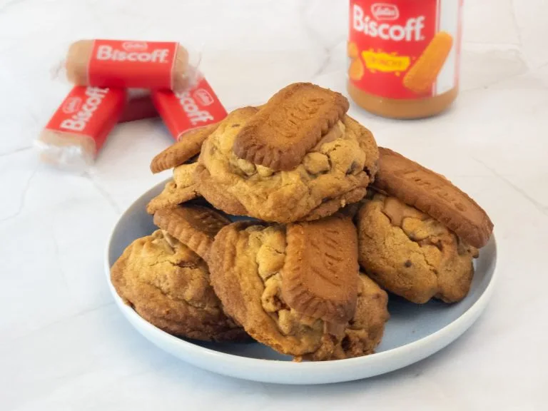 A plate of Deluxe Biscoff Loaded Cookies with Biscoff cream and biscuit packs in the background, showcasing the rich caramelised flavour.