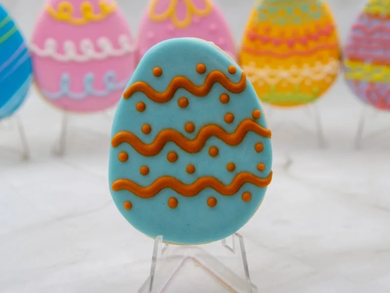Close-up of an individual Easter Egg Wonderland Cookie with orange icing and zigzag patterns.