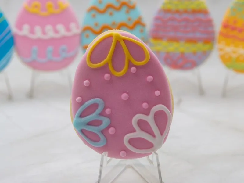 Close-up of an individual Easter Egg Wonderland Cookie with pink flower and swirl decorations, made with royal icing.