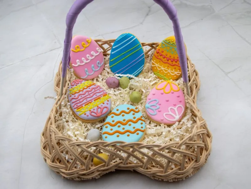 Easter Egg Wonderland Cookies beautifully arranged in a woven basket, showcasing vibrant royal icing designs.