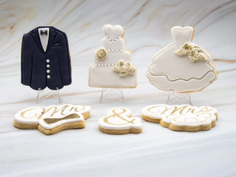 Bridal gown, wedding cake, and tuxedo cookies standing vertically with fondant decorations and gold accents.