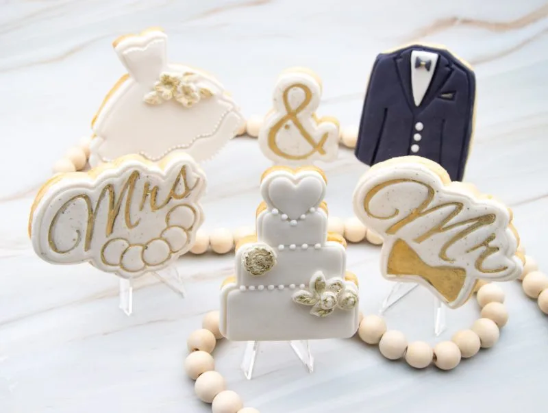 Wedding gown and tuxedo wedding cookies standing vertically with fondant detailing and gold accents.