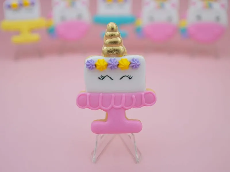 Unicorn birthday cake cookie on pink stand with purple and yellow flowers