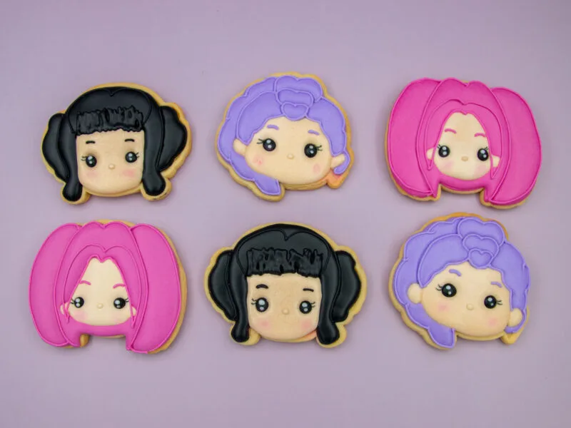 Flat lay of Kpop Huntrix royal icing cookies in pink, black and purple hair designs