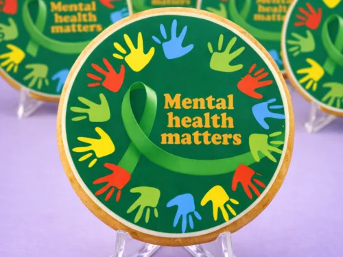 Close up of Mental Health Awareness Cookie with green ribbon and colourful handprint edible print design