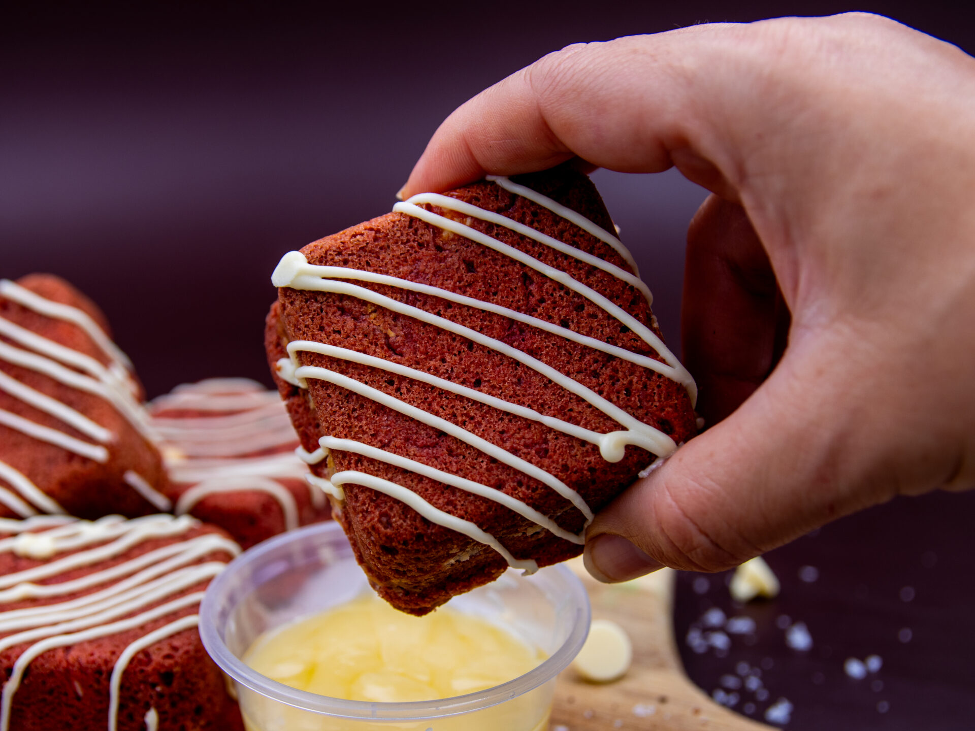 Hand holding Red Velvet Cream Cookie Cube above white chocolate dip